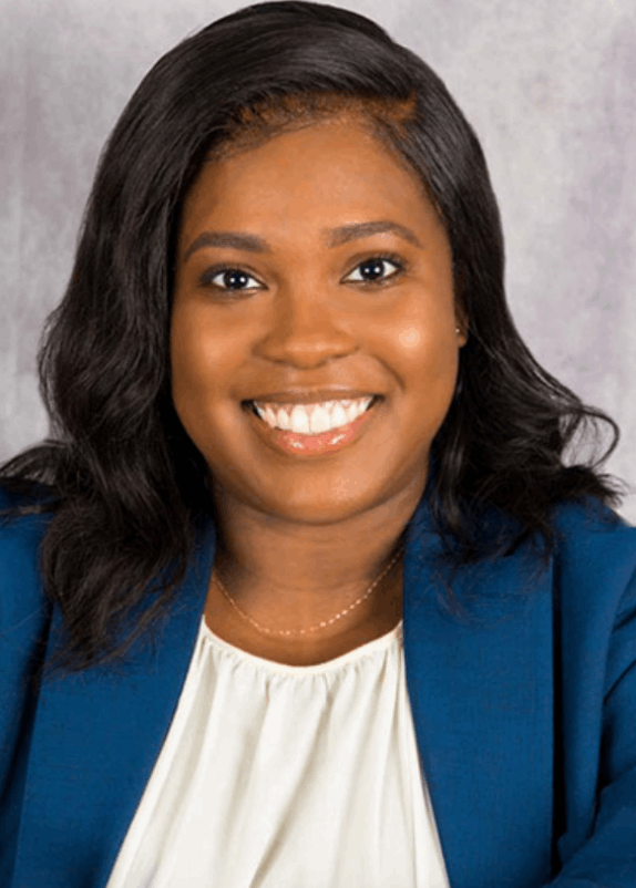 Smiling Black woman with shoulder-length wavy hair wearing a professional blue blazer and white blouse.