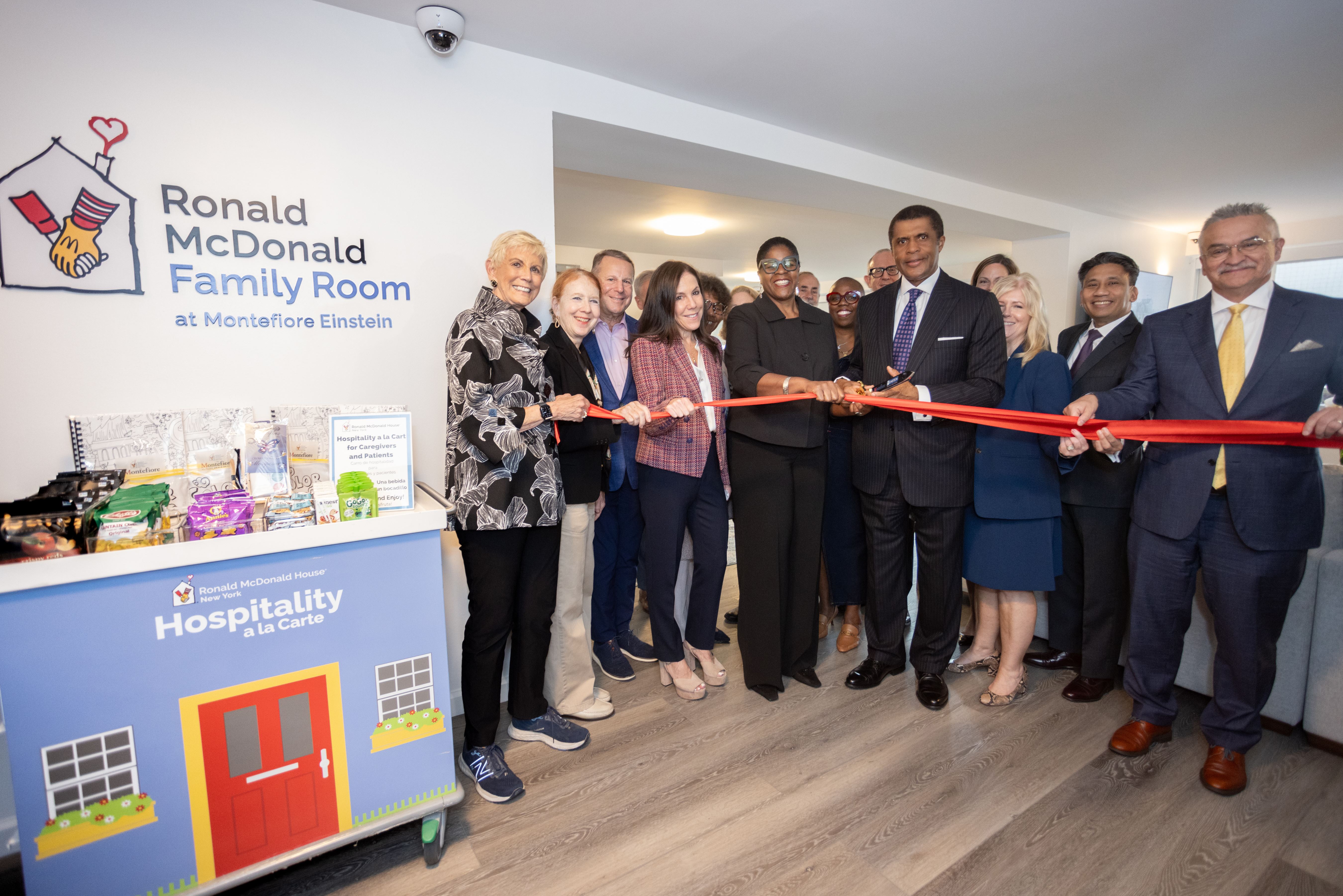 Smiling boy in a hospital bed with a tracheostomy tube and bandaged hand, holding a tan teddy bear.